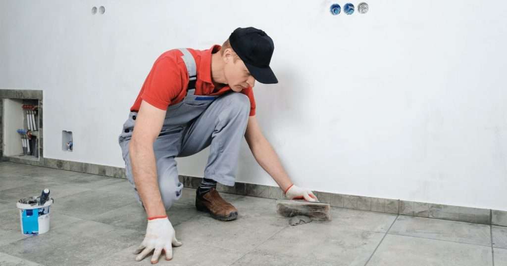 A man with red shirt, black hat and Grey paint - applying the grout on floor project